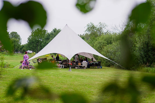Balta zvaigznes telts uzstādīta zālienā, piemērota viesu zonai vai lounge vietai.